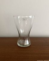 Clear glass vase with a gently flared opening tapering into a narrower base, shown against a plain backdrop.