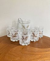Front view of the vintage Italian frosted glass ice bucket with gold leaf pattern and six matching drinking glasses arranged on a wooden surface.
