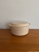 Full view of the vintage cream-colored melamine casserole dish with lid on a wooden surface.