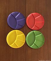 Four round melamine plates in purple, red, yellow, and green with three small and one large compartment.