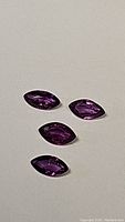 Four marquis cut deep purple sapphires arranged on a white surface showing color and cut.