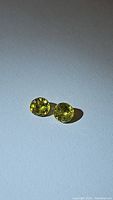 Pair of round cut sphene gemstones with yellow-green color on white background with clear detail of facets and brilliance