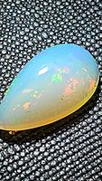 Close-up front view of the pear-shaped Ethiopian opal displaying its multicolored play of color on a black textured background.
