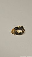 Natural pear cut golden citrine gemstone photographed against plain background showing facets and color.