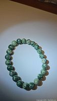 Photo of a stretchy bracelet made of round green spotted jasper beads, approximately 8mm size, displayed on a flat surface.