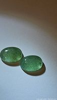 Two oval green strawberry quartz cabochons placed on a white background showing color, shape and surface condition.