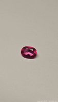 Close-up photo of the natural hot pink oval cut topaz gemstone on a neutral background showing its clarity and facet detail.
