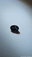 Oval cut deep blue sapphire gemstone showing facets and shadow on white textured fabric.