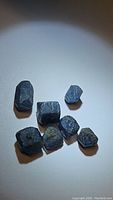 Seven rough natural blue sapphire crystals of different sizes, showing their uncut, semi-transparent blue appearance with some inclusions.