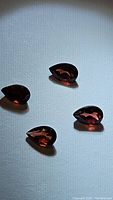 Four pear-shaped deep reddish garnet gemstones placed on a white surface showing facets and color under light.