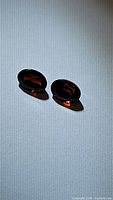 Photo showing two oval cut deep red garnet gemstones placed on a white surface with shadows visible, bright natural light highlighting facets.