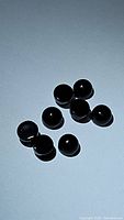 Ten small round black cabochon stones arranged on a flat surface as seen under direct light.