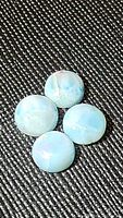 Four natural Larimar round cabochons with soft blue color and white matrix on black fabric background.