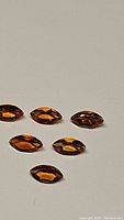 Six marquis cut deep orange-brown Madeira citrine gemstones laid out on plain light background, showing facets and color depth