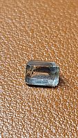 Top-down view of light green prasiolite green amethyst emerald cut gemstone on brown textured background