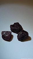 Three rough natural red ruby crystals on white background, showing deep reddish color, uneven uncut surfaces, and semi-transparency.