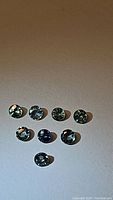 Seven round cut natural blue-green sapphires arranged in a row with clear reflections, shown on neutral background.