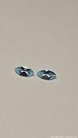Two marquis cut sky blue gemstones displayed on a neutral surface.