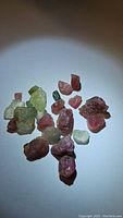 Photo of multiple rough mixed color tourmaline crystals in pink, light green, and dark green shades, showing the natural uncut form.
