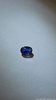 Oval blue kyanite gemstone on a plain background, showing color and internal inclusions.