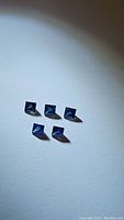 Five princess cut blue sapphires arranged on a surface, showing size and shape consistency.