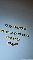 24 round faceted sapphire gemstones in varied rainbow colors displayed on a flat surface.