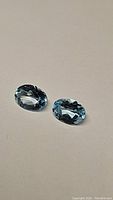 Two oval faceted sky blue topaz gemstones on a plain background showing size, shape and color.