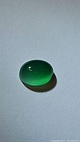 Oval vivid green Onyx cabochon gemstone on a plain background, showing polished smooth surface and vibrant green color.