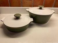 Both casseroles with lids on showing olive green bottoms and white lids with matching knobs