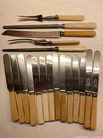 Full lot showing 7 serving/cutting utensils above 12 butter knives