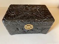 Front view of carved black lacquered box showing bird and floral relief and brass clasp