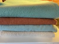 Stack of four folded wool blankets showing color range: light aqua, rust, pale blue, cream