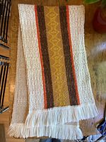 Folded table runner showing cream ribbed weave, multicolour stripes, fringed end