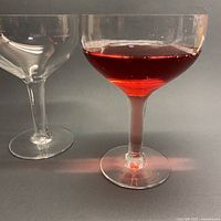 Side view of two champagne coupes, one with red liquid highlighting hollow stem