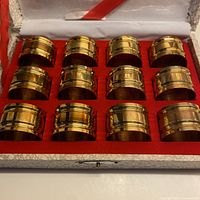 Open presentation box showing all twelve brass napkin rings in red felt insert