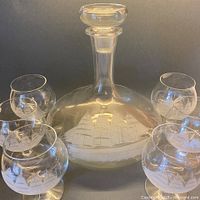 Full decanter with stopper surrounded by six etched glasses