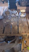 Eight used mason jars on wooden pallet, clear glass with various metal lids, light wear visible.