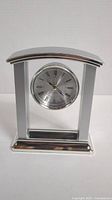 Front view of silver-tone alarm clock with Roman numeral face and polished metal frame.