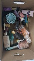 Full view of various beauty products including bottles, tubes, hairbrushes, and a blue flower candle holder inside a cardboard box.