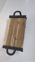 Top view of a rectangular wooden charcuterie board with a natural finish and black metal handles on either side.