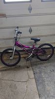 Full side view of purple kids bicycle with 16-inch wheels, black tires and purple rims in a garage.