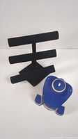 Black velvet T-bar jewelry display holder next to blue and gold necklace display stand with bracelet and fake necklace