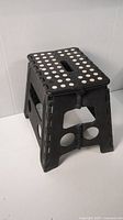 Side angle showing the black folding step stool with white anti-slip dots and handle opening on top.