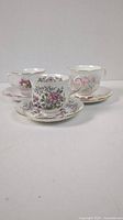 Three floral porcelain teacup sets with saucers arranged side by side showing different floral patterns and gold trim.