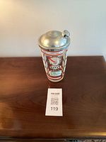 Front full view of 1950s Hazel Atlas cocktail shaker on wood surface with metal lid and printed cocktail recipe artwork.