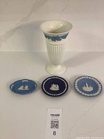 4 vintage Wedgwood pieces: a white and blue jasperware vase and three small jasperware plates in blue tones with classical white reliefs displayed on a white surface.