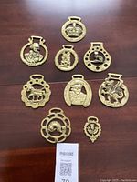 Full lot of 9 vintage brass horse buckles displayed on wooden surface.