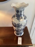 Full frontal view of tall white pottery vase with blue toile design and flared rim, standing on wooden surface.