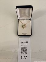 Front view of heart-shaped emerald and diamond pendant necklace displayed in an open jewelry box marked '18 KT gold over sterling silver'.