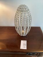 Front and angled view of an egg shaped votive candle holder with metal frame and circular clear crystal embellishments, showing its size and design.